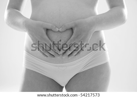 Belly of pregnant woman with fingers showing heart