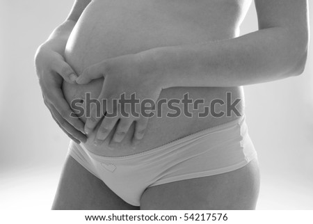Belly of pregnant woman with fingers showing heart