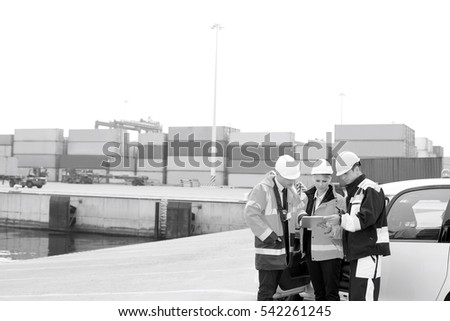 Workers using tablet PC beside car in shipping yard
