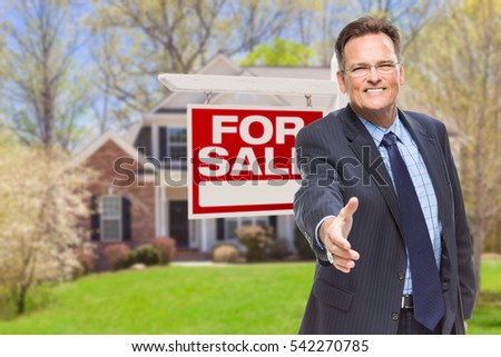 Smiling Male Agent Reaching for a Hand Shake in Front of Beautiful House and For Sale Real Estate Sign.