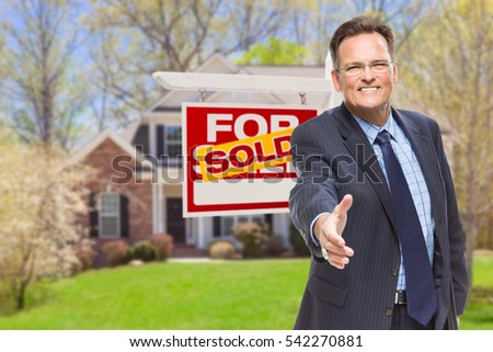 Smiling Male Agent Reaching for a Hand Shake in Front of Beautiful House and Sold Real Estate Sign.