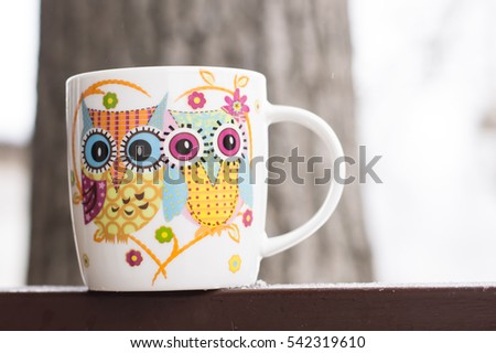 Winter. Mug for tea with a picture of owls on the background of snow-covered yard.