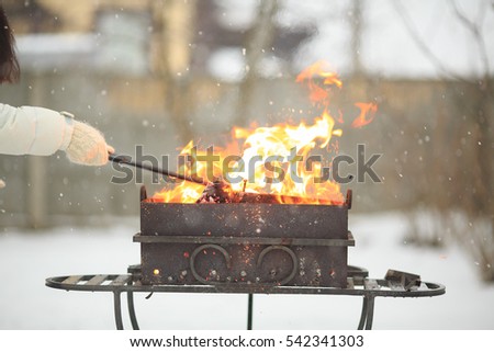 Hand with poker adjusts the coals in the brazier. Lighting the barbecue in the backyard in the winter.