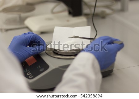 Scientist putting drugs on digital weighing scales. Medical blue gloves and white uniform on a person.