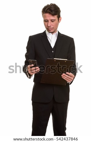 Studio shot of handsome Caucasian businessman using mobile phone while holding clipboard isolated against white background