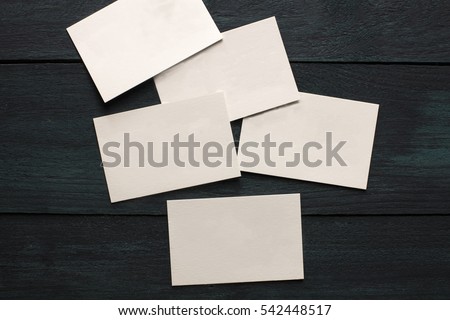 A photo of blank white thick cardboard business cards on a dark wooden background texture. A mockup or a minimalist banner with copyspace