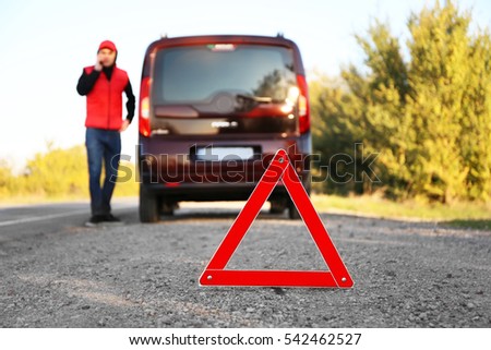 Red warning triangle on asphalt road. Driver near broken down car calling for help