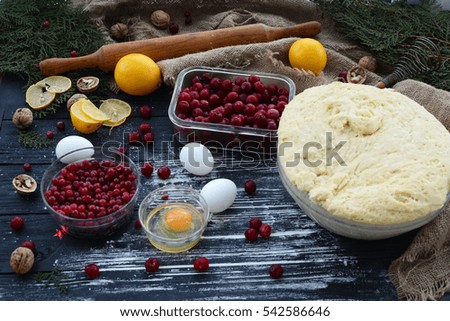 Cake during cooking. Dough, flour, cherries, cranberries, lemons, eggs, nuts, and kitchen utensils on a black wooden table