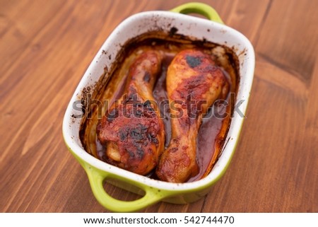 Chicken drumsticks marinated in soy sauce, honey, beer and tomatoes and than roasted in small ceramic roasting pan. Close up Picture served in the pan without any side dish or salad.