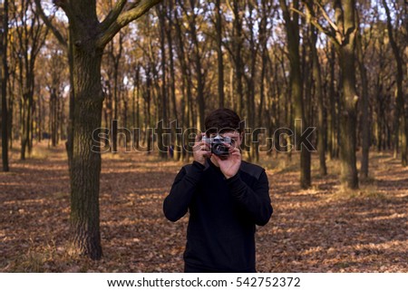 Young handsome man photographing on old retro camera in a forest in autumn.
