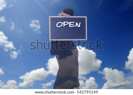 A women holding a chalk board with word " OPEN " isolated in a background of blue sky.