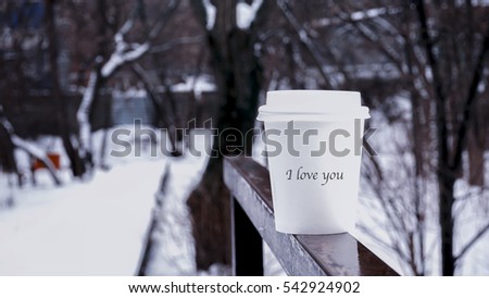 glass of coffee on a railing, a word on a paper sticker i love you