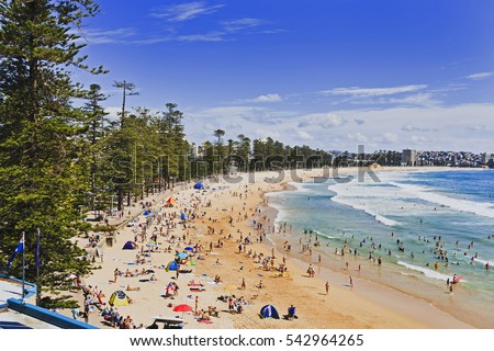 Sydney northern beaches main Manly beach facing pacific ocean on a sunny summer day with crowd of tourists and beachgoers relaxing and sufring. Royalty-Free Stock Photo #542964265