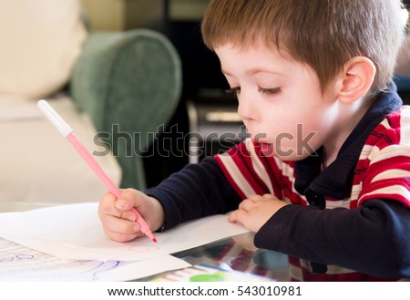 Beautiful child boy sits and draws with opened mouth