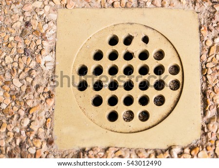Wet outdoor tile floor drain hole close up.