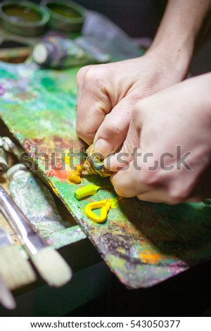 hands of artist mix paints on a palette. composition on a dark background 