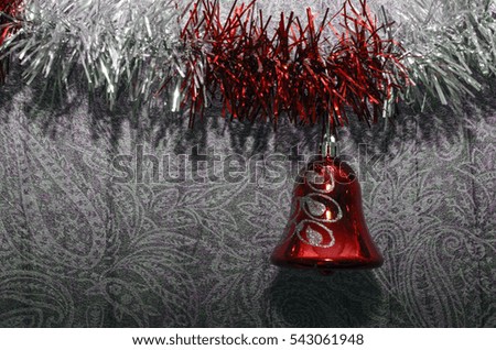 Closeup of red maroon pink violet glass toy bells hanging from a decorated Christmas silver purple red maroon colored tinsel on grey patterned wallpaper  background, New year greeting card or poster