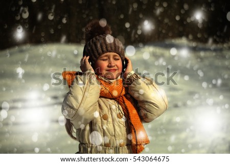 Winter girl standing under falling snow and listens to music, background for a card.