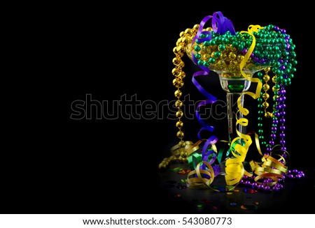 Mardi Gras image of purple, green and gold beads and ribbons spilling out of a party drink glass on black background. Copy space.