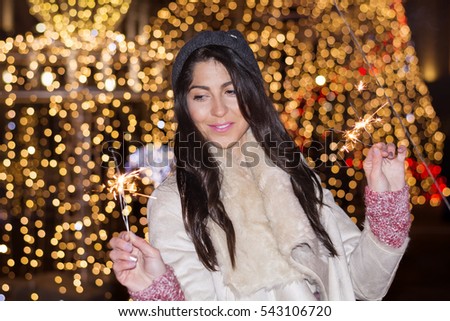 Beautiful smiling young woman  holding a sparkler on a New Year's Eve.Night scene with lights