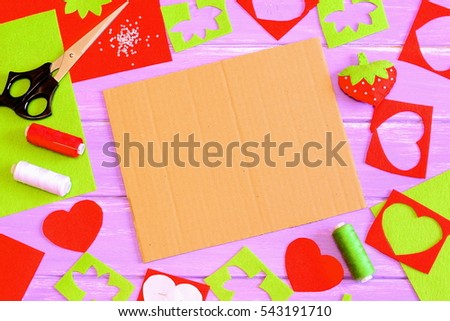 Sewing and cutting handicraft background. Summer red felt strawberry toy, scissors, felt sheets and scraps, paper pattern on wooden background. Cardboard sheet with copy space. Summer background table
