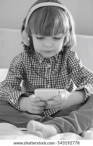 Full length of cute boy listening music on headphones in bedroom