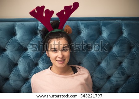 Beautiful girl. Girl with reindeer horns. A girl sits on a blue couch with ornament. Girl with horns on the couch