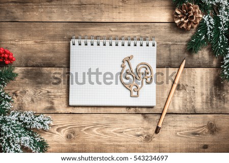 Blank paper notebook and yellow pencil on brown wooden table background with branch of a Christmas tree, pine cones and rowan. Top view with copy space.