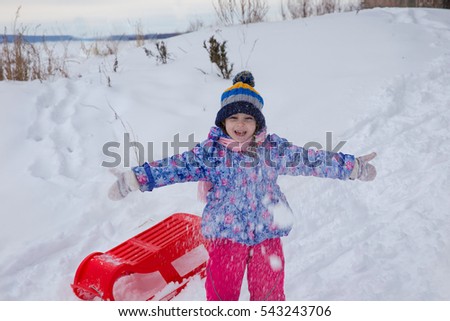 little 5 year old girl in winter jacket with red sleds, plays on the Playground in winter Park