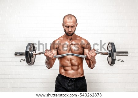 Studio portrait of handsome topless bodybuilder doing exercise on biceps against white background.