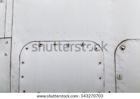  metal surface of old unused airplane gray. In paint, some visible damage, as well as metal rivets and bolts connecting the sheets of material. Small depth of field.