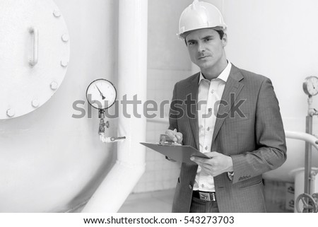 Portrait of confident young male inspector writing on clipboard in industry