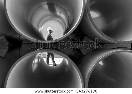 Full length side view of young male architect walking by stacked pipes at construction site