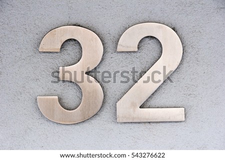 Number 32 in stainless steel on a white plaster wall
