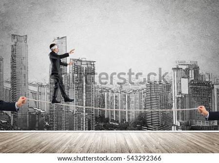 Businessman with blindfolder on eyes walking on rope