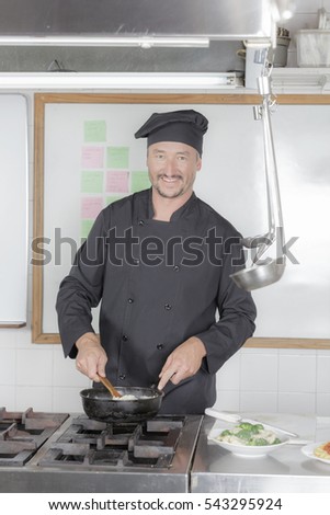 Mature male chef in black uniform preparing a meal in a hotel industrial kitchen