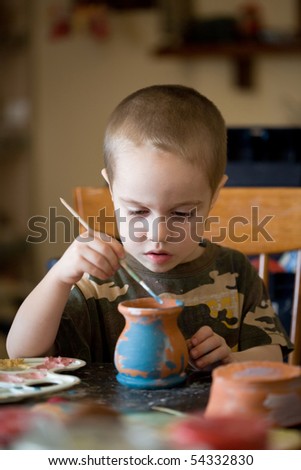 small boy paints the clay jar