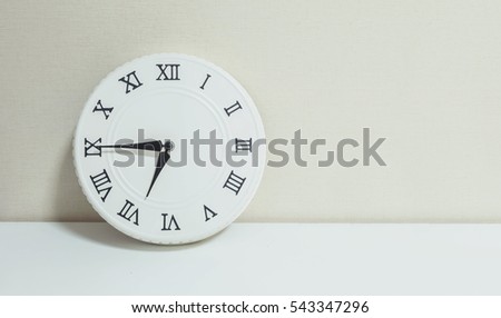 Closeup white clock for decorate show a quarter to seven or 6:45 a.m. on white wood desk and cream wallpaper textured background with copy space