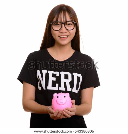 Young happy Asian nerd teenage girl smiling and holding piggy bank