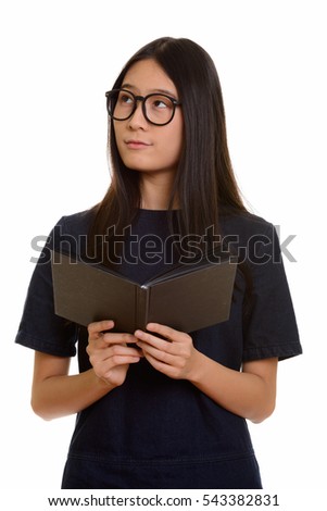 Young beautiful Asian teenage girl holding book while thinking
