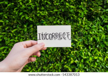 hand holding "incorrect" card on green leave background