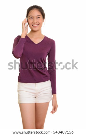 Young happy Asian teenage girl smiling and talking on mobile phone while thinking isolated against white background