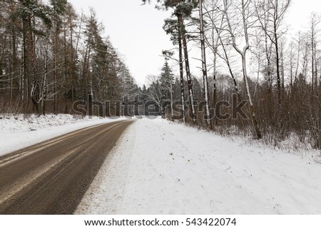   Traces left by car on the snow-covered road in the winter season. Photo closeup in cloudy weather. The road passes through the forest with trees