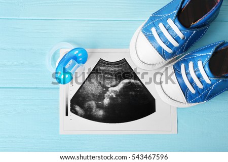 Ultrasound photo, baby boots and pacifier on blue wooden background