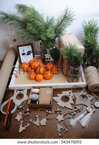 The general plan of the table with Christmas decor. Christmas tree branch in a glass carafe. Gift wrapping with kraft paper, pendants and jute. Tangerines with cloves, tied with a cord