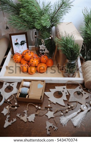 The general plan of the table with Christmas decor. Christmas tree branch in a glass carafe. Gift wrapping with kraft paper, pendants and jute. Tangerines with cloves, tied with a cord