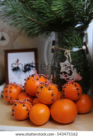 Tangerines, decorated with cloves and red-white lace. Close-up on a background of fur-tree branches in a glass vase with a wood star and deer. Rooster picture framed
