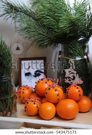 Tangerines, decorated with cloves and red-white lace. Close-up on a background of fur-tree branches in a glass vase with a wood star and deer. Rooster picture framed