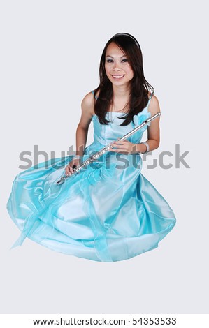 A young Asian woman in an light blue evening dress holding the flute sitting on the floor in the studio for light gray background.