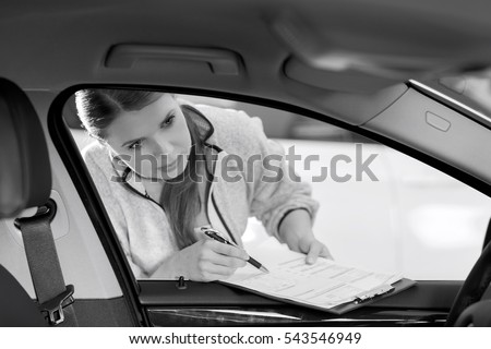 Female maintenance engineer with clipboard examining car's interior in workshop
